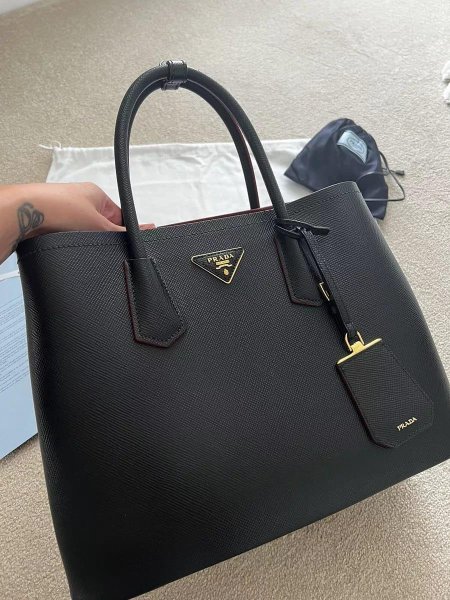 حقيبة يد فاخرة من Prada بتصميم أسود كلاسيكي وخامة أنيقة متينة، تجمع بين البساطة الراقية والعملية اليومية. خيار مثالي لإطلالة أنثوية فخمة تعكس ذوقًا عصريًا وثقة عالية.