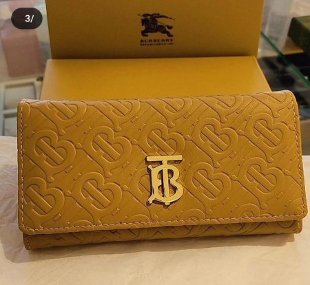 محفظة أنيقة من Burberry بلون ذهبي فاخر مع نقش المونوغرام الأيقوني وشعار معدني راقٍ. تصميم عملي وأنيق يضفي لمسة فخامة على إطلالتك اليومية ويجمع بين الذوق الكلاسيكي والعصري.