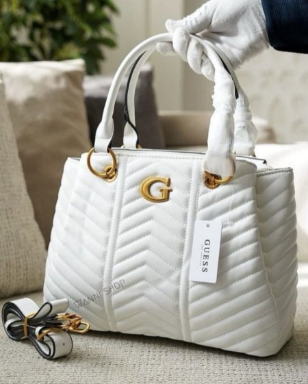 حقيبة نسائية فاخرة بتصميم مبطّن أنيق من GUESS، بلون أبيض راقٍ مع تفاصيل ذهبية تضيف لمسة فخامة. واسعة وعملية مع حزام كتف قابل للإضافة، مثالية للاستخدام اليومي والمناسبات بإطلالة أنثوية عصرية.